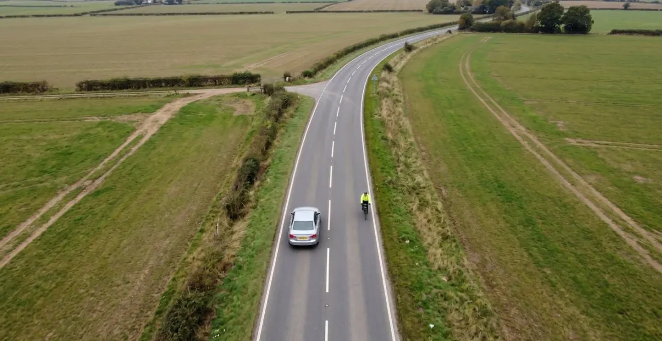 Vue aérienne d'une voiture dépassant un cycliste sur route de campagne avec marquage au sol